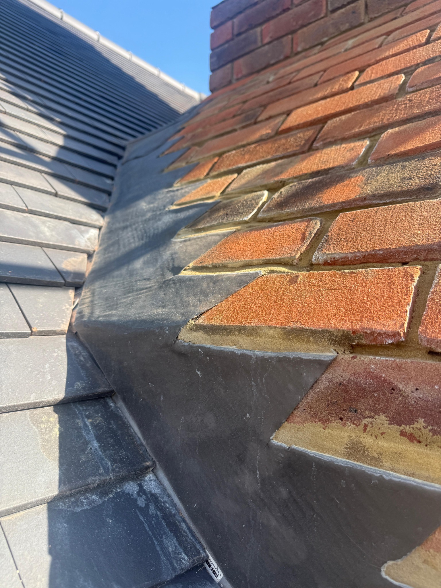 Stepped metal flashing where roof tiles meet a brick chimney